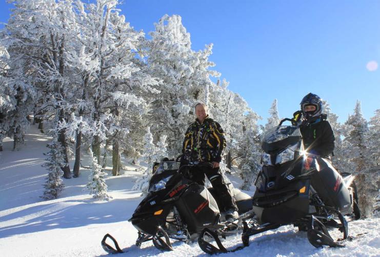 Two riders standing on their parked snow mobiles