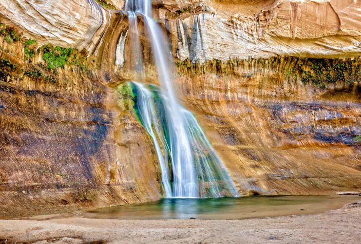Lower Calf Creek Falls drop into a pool with a mossy cliff wall.