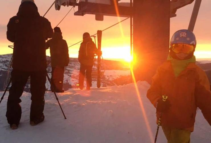 Skiers at top of the mountain with sunset behind