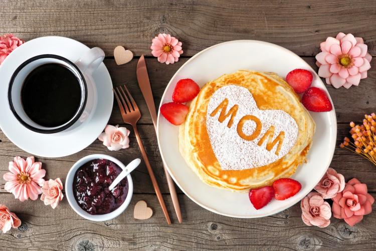 Pancakes with 'MOM' in powdered sugar, coffee, utensils, pink flowers