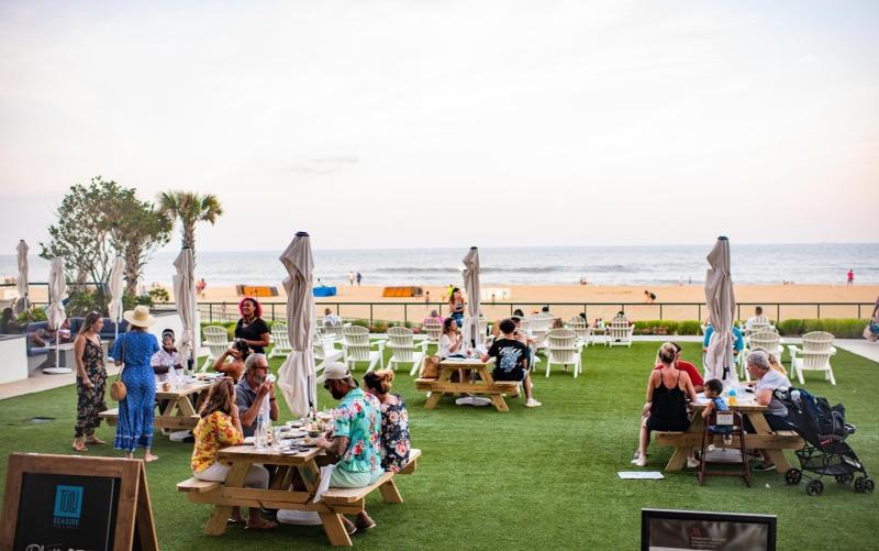 outdoor restaurant seating area on a grassy patch overlooking the ocean with picnic tables and people dining