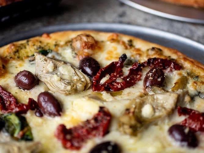 Image of a pizza with red beans, cheese, sun dried tomatoes and artichokes.