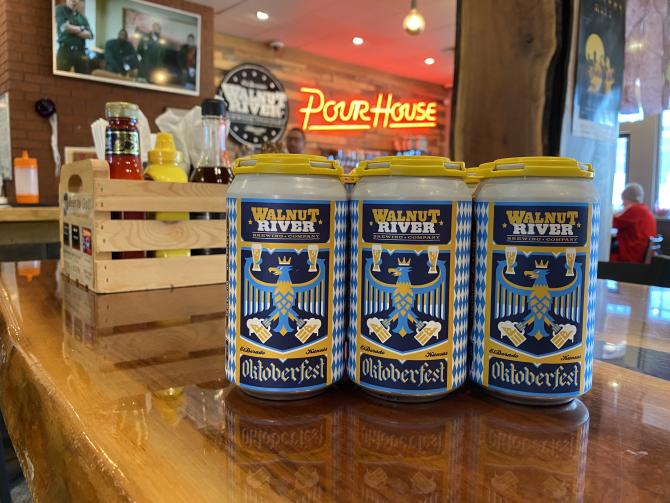 Three cans with blue and white striped designs and the words "Walnut River Oktoberfest" sit on a bar top in the Walnut River Pour House
