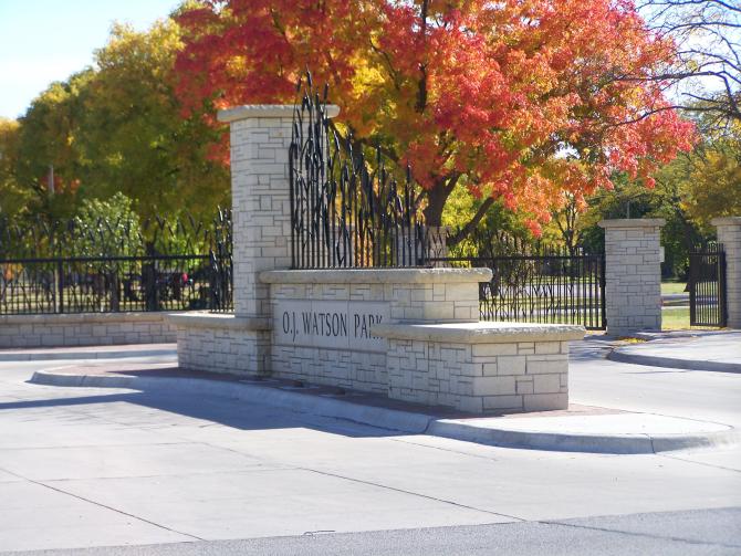 The white-hued entryway at OJ Watson Park in Wichita, KS, set apart from the red and yellow leaves on the tree behind it