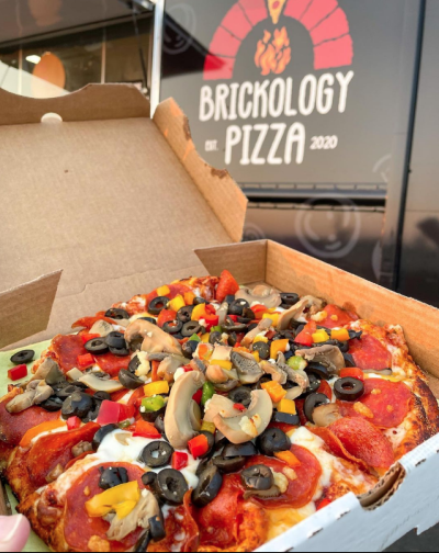 Person hold pizza box with pepperoni, mushroom and olive pizza in front of food truck