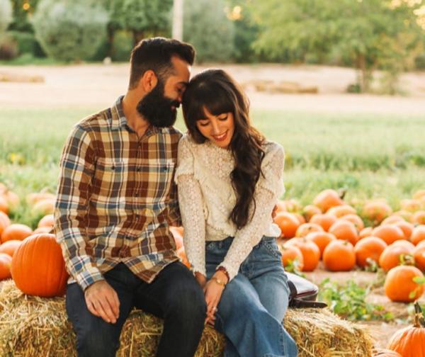 A young couple sits on a hay bale in front of a pumpkin patch at the Twin Cities Harvest Festival & Maze