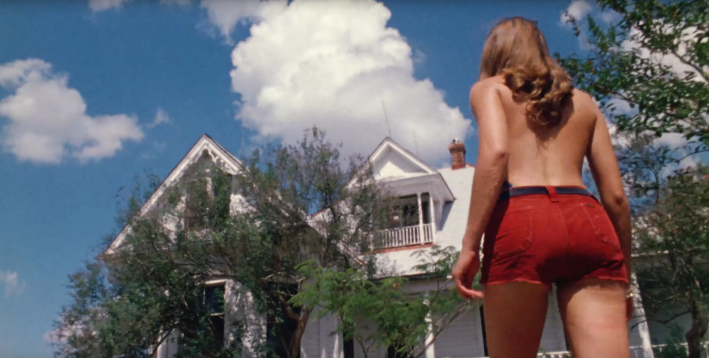 Texas Chainsaw Massacre screengrab, showing a topless woman in red shorts walking towards a white house