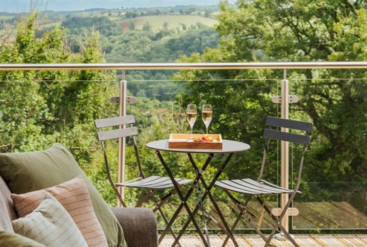 two glasses of champagne sat on a table, with two chairs facing each other on a balcony at The Mole Resort