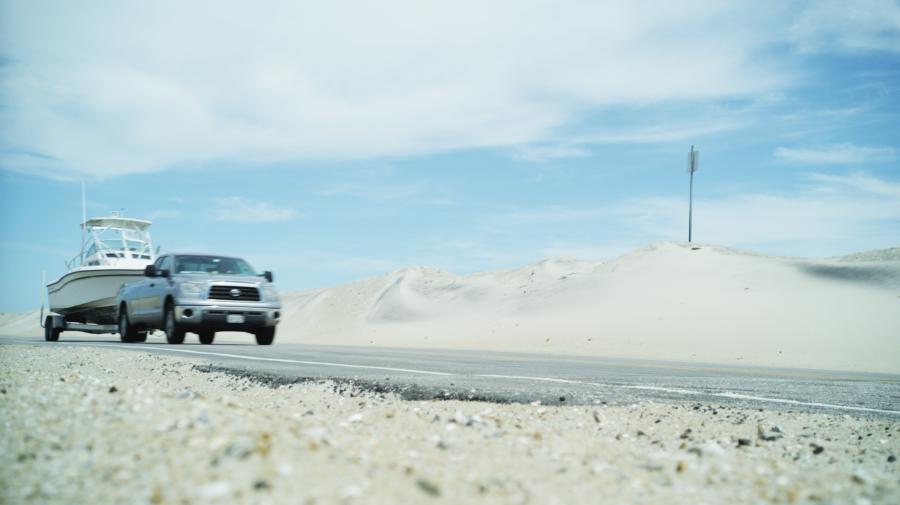 A truck with a boat on a trailer travels along Highway 12 of the Outer Banks in NC