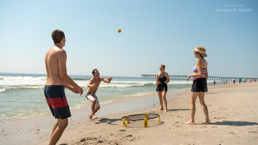 a group of four people playing a game with a small ball and a net on the beach