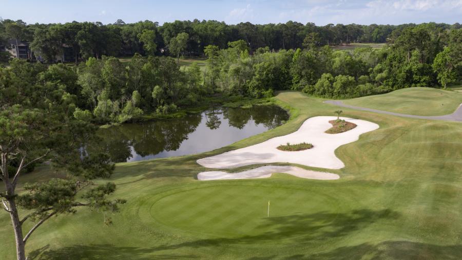 an aerial view of a golf course green and bunker by a pond of water at Jones Course at Sea Trail