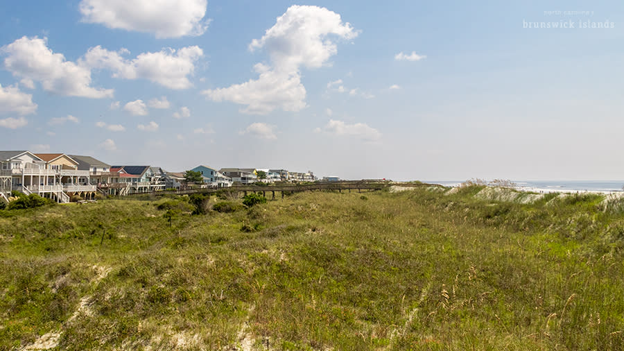 a row of houses behind sand dunes on a beach
