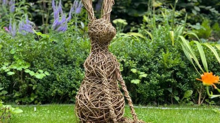 A large willow hare stands in a garden with orange and purple flowers in the borders