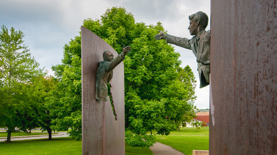 two statues of Martin Luther King Jr and Robert Kennedy reaching for one another. Trees and blue skies in background