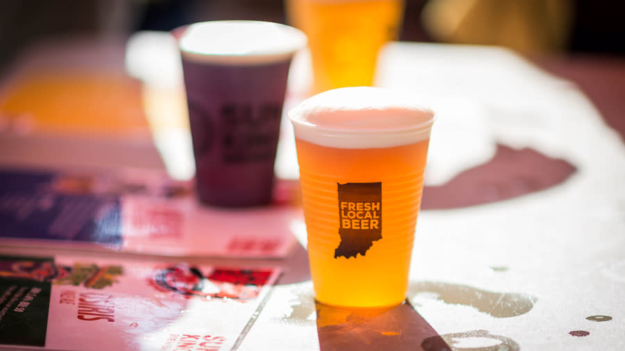 Two plastic cups of beer, one reads "Fresh Local Beer" on a graphic of Indiana