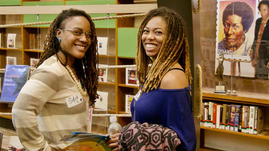 Two Black Women smiling with bookshelves behind them