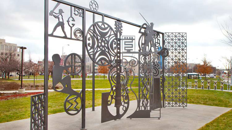 A iron sculpture showing people performing various activities - biking, playing baseball, playing the violin,