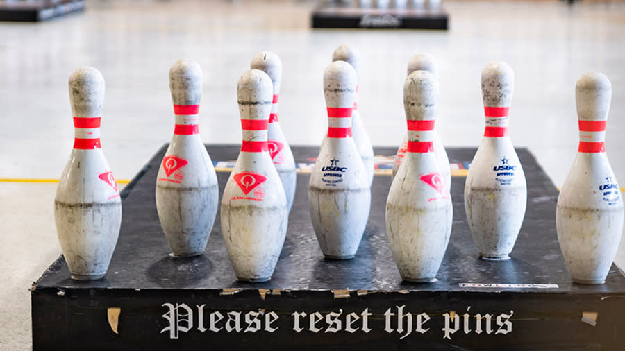 a group of bowling bins in a row. Sign reads "Please reset the pins"