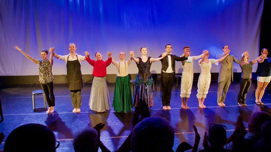 A group of actors standing in stage and holding their hands in the air