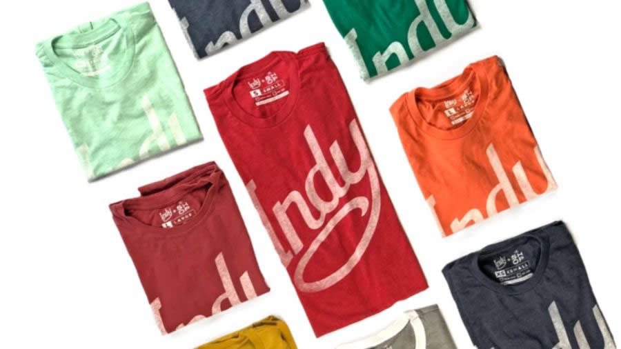 multiple Indy-branded tees folded next to each other. Red, Green, Blue, Grey, Orange, Mint