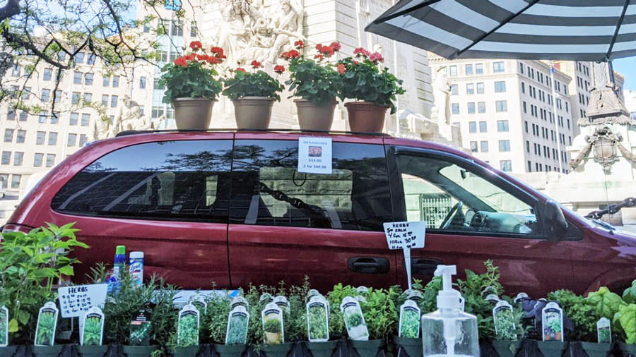 a red minivan with flowers on top and plants being sold in front of the van. Images is taken in downtown indianapolis by the Soldiers & Sailors Monument. 
