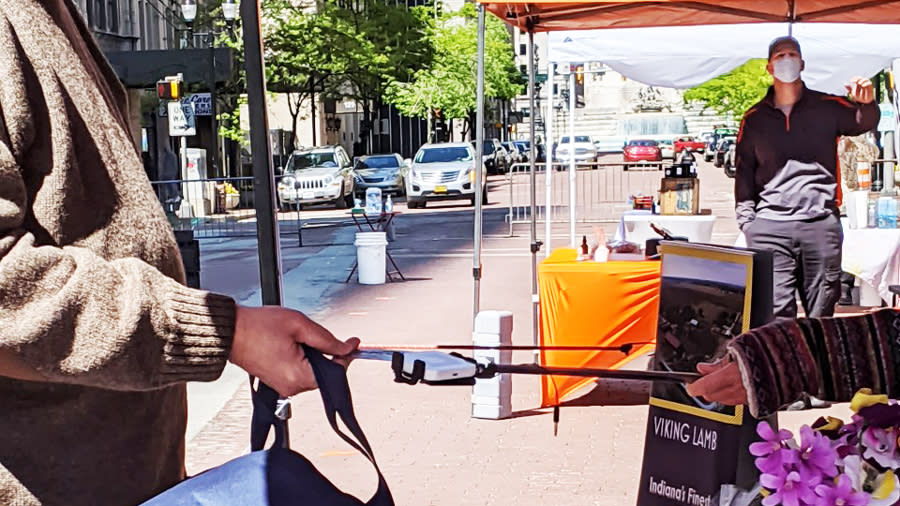 A man paying for his purchase using an elongated stick to pay. A man in the background is wearing a mask. 