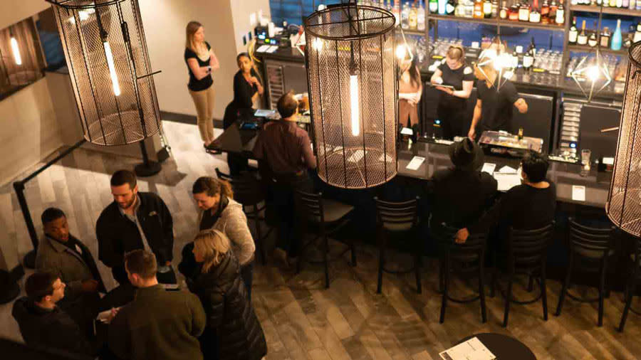 Bar scene at Helium Comedy Club. Patrons are standing and being served drinks. 