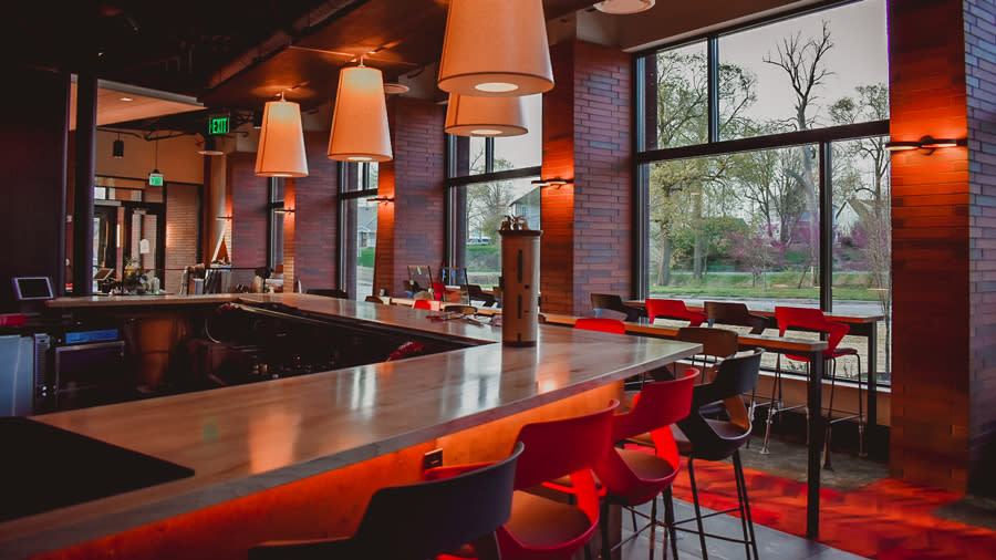 Kan Kan bar inside. Hanging lights line a bar top with chairs and windows behind.