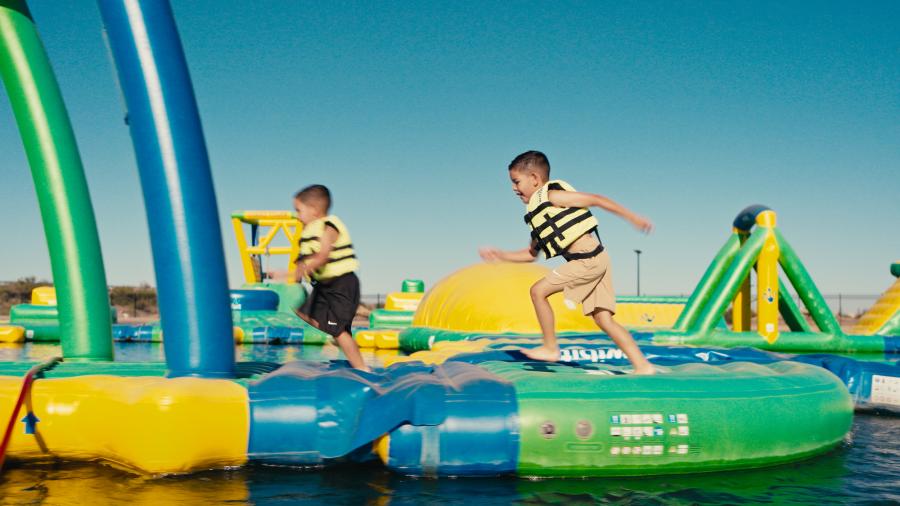 Two little boys with lifejackets play on an inflatable water park in Deming, New Mexico