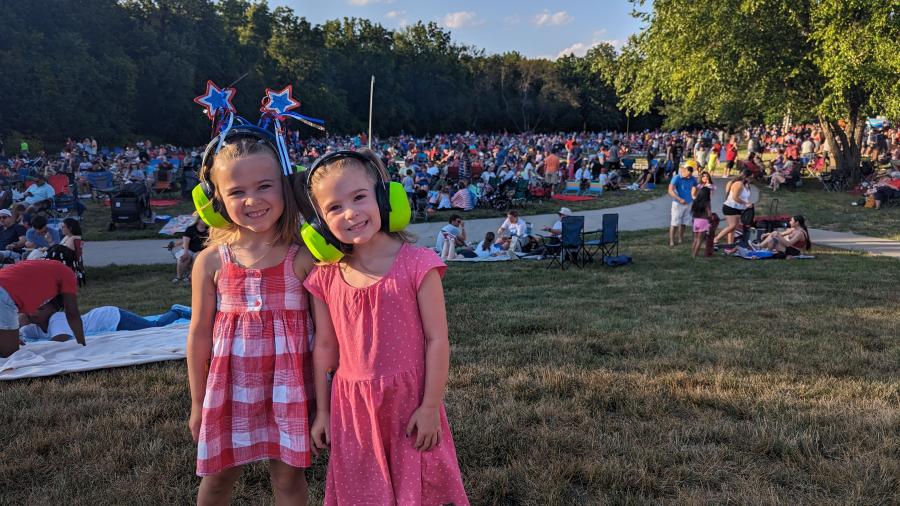 Two girls pose with noise-cancelling headphones on at the City of Overland Park's Star Spangled Spectacular event at Corporate Woods Founders' Park.