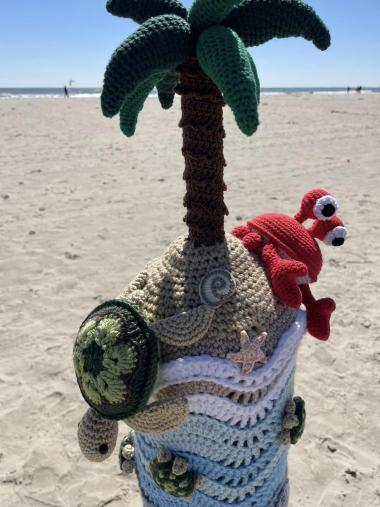 Close up of a crocheted bollard buddy showing a palm tree, a crab, a turtle, water, and more.