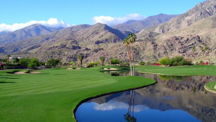 Indian Canyons Golf Resort featuring bright green fairways, reflective water hazards, and dramatic mountain views under a clear Palm Springs sky.