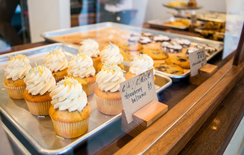 Cupcakes and cookies sit on metal trays behind the glass at Two Sticks in Bloomington.