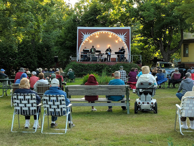people sit in a park listening to live music from a bandshell