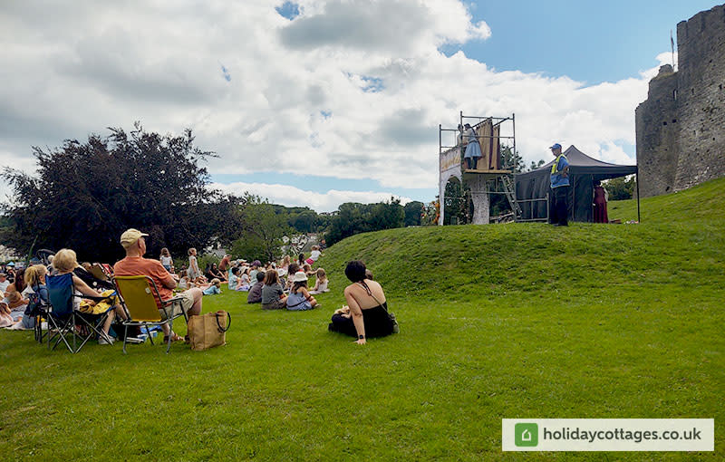 People sitting on the grass outside Oystermouth Castle watching a play.