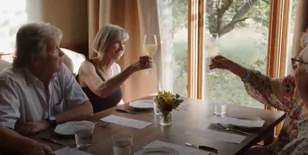 Two women toast their glasses of white wine at a table at Edlerslie Farm