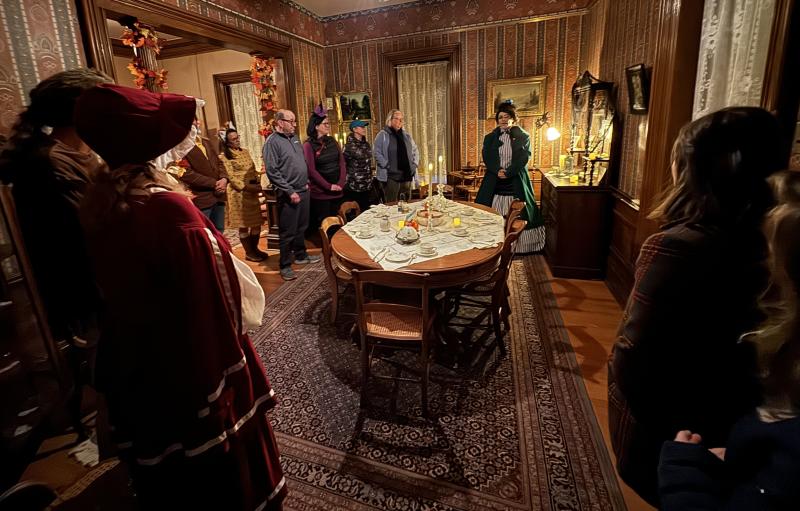 People gathered around a historic table with candles around and the tour guide dressed in period appropriate clothing