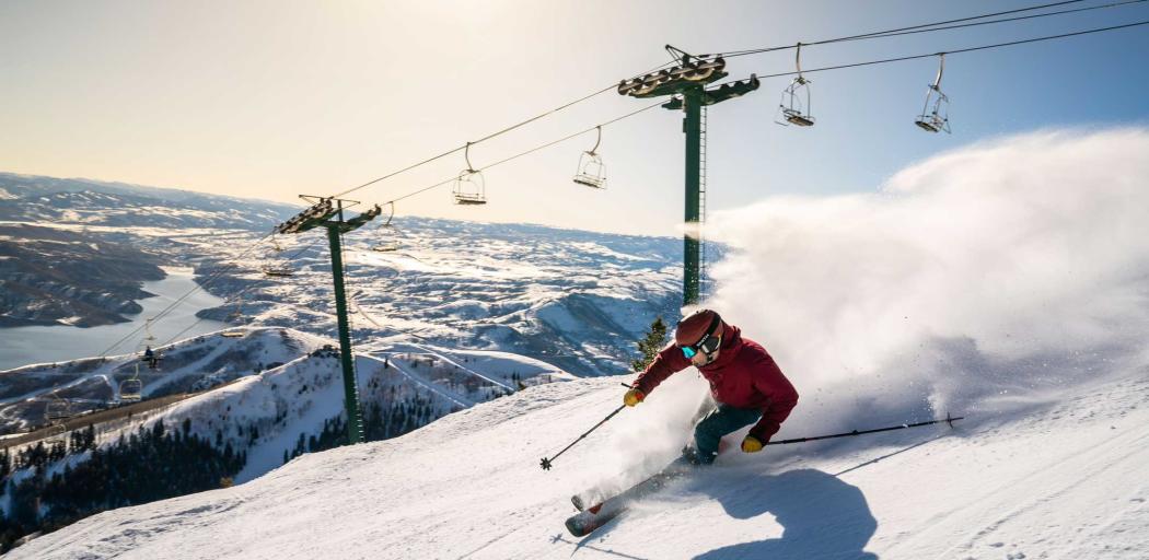 A skier carves a turn in front of a rising sun and chair lift at Deer Valley in Park City, UT