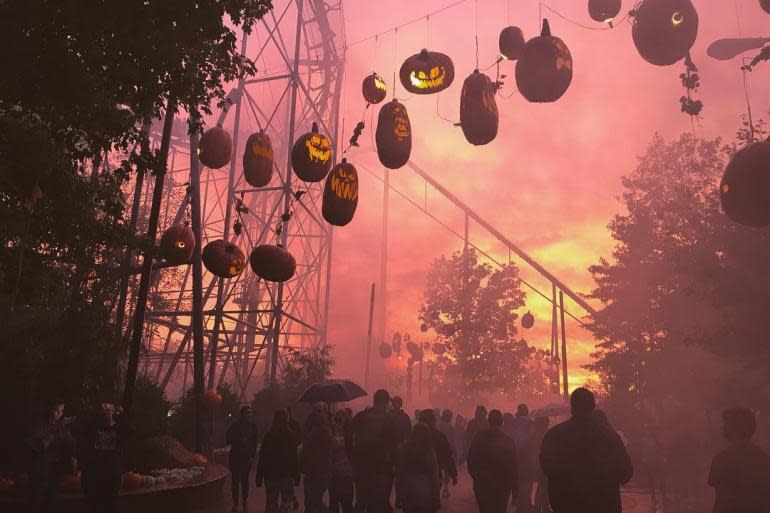 Jack o Lanterns hanging over a sidewalk full of people with a pink and yellow sky