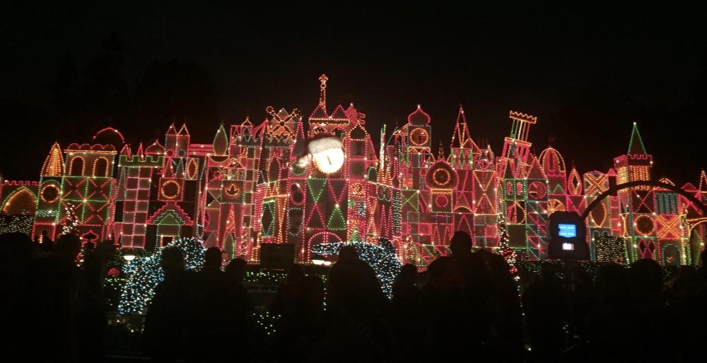 The front of the "It's a small world" attraction at Disneyland lit up in holiday lights that shine white, red, and green.