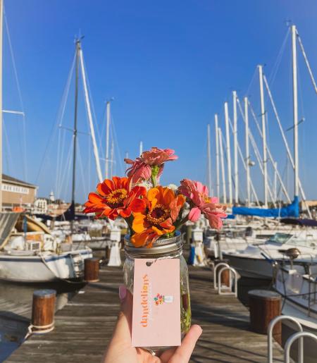 A vase of Zinnias with Sailboats and a pier in the background