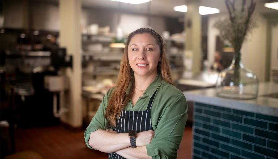young woman in a green blouse and black and white striped apron standing in a restaurant kitchen