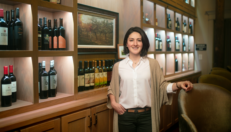 Young brunette woman standing in bar with wine bottles on shelves behind her