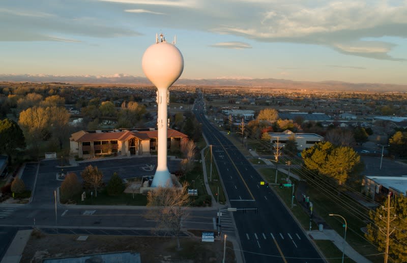 This image depicts an aerial view of Greeley, Colorado, with a water tower at the center of the photograph.  The water tower sits at the intersection of two roadways, which are lined with trees and buildings.