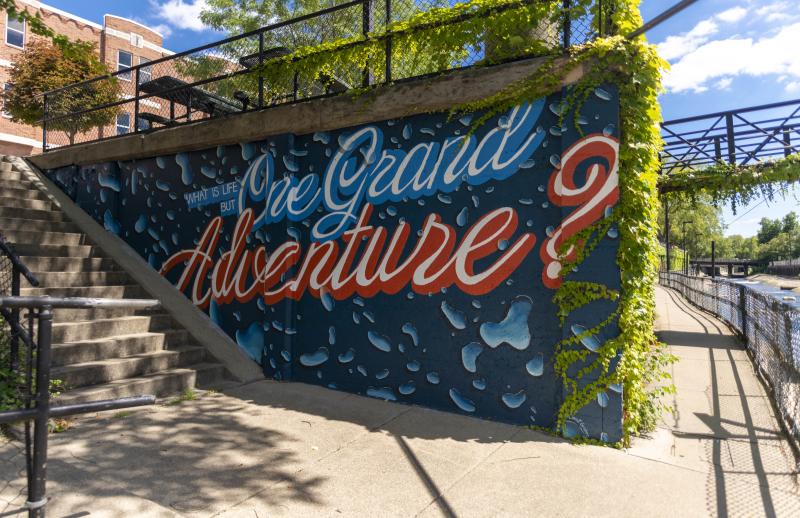 Painted mural along the East Race Waterway that states, "What is life but one grand adventure?"