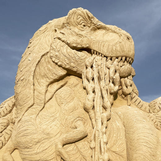 Up-close of a sand sculpture showing a T-rex with unidentifiable substance in its mouth