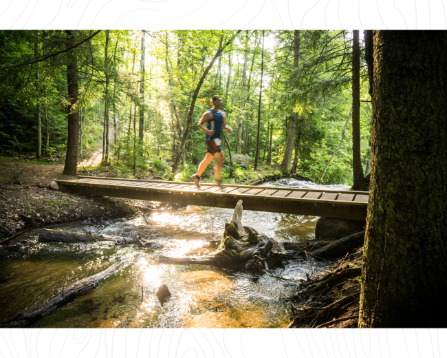 A runner crossing a wooden footbridge on the forested NTN South Trails