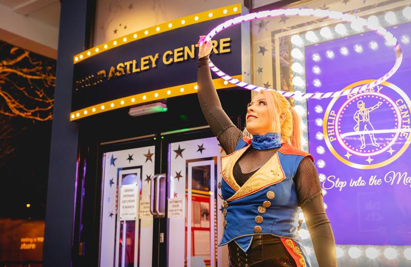 A circus performer prepares to entertain with some spectacular hula hoop tricks, outside The Philip Astley Centre at night
