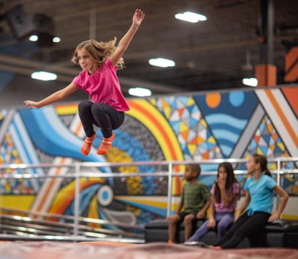 A young girl jumping on a trampoline while her friends sit nearby