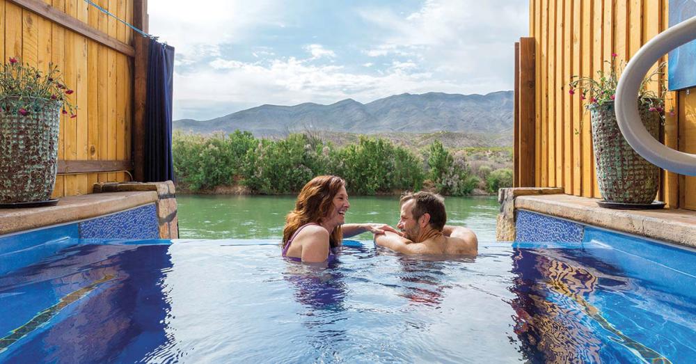 A couple enjoys a relaxing moment in Riverbend’s infinity pool overlooking lush greenery and distant mountains.